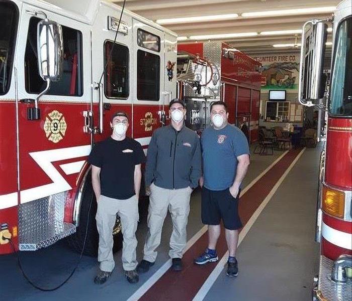 Three men standing in front of a fire truck. 