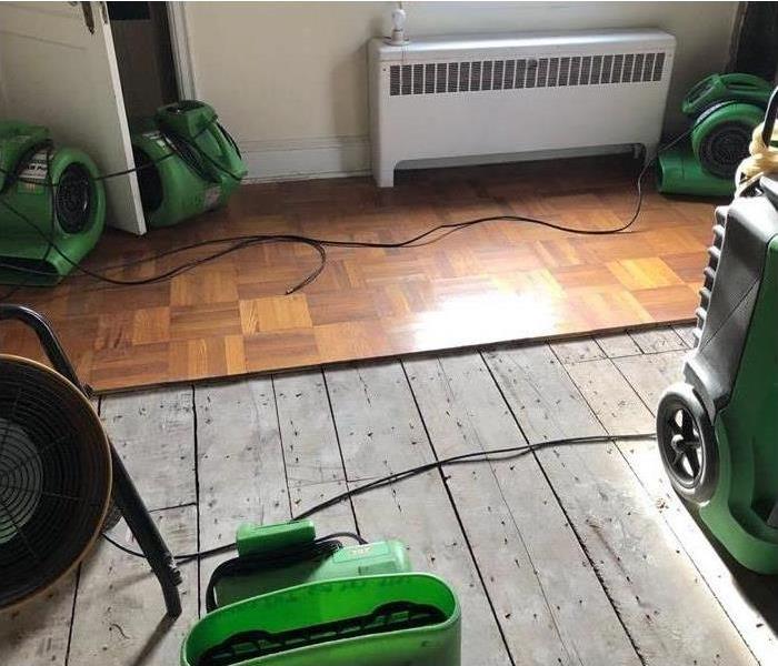 Half of wood flooring removed, air movers placed on a room